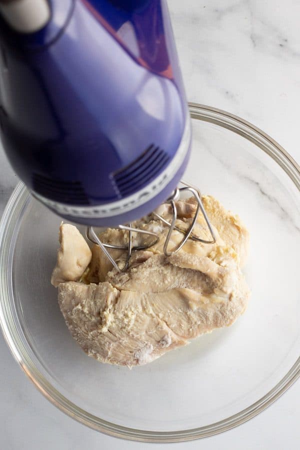 Blue handheld mixer shredding chicken breast