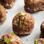 Baked meatballs on a sheet pan topped with chopped herbs.