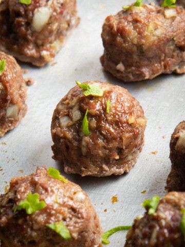 Baked meatballs on a sheet pan topped with chopped herbs.