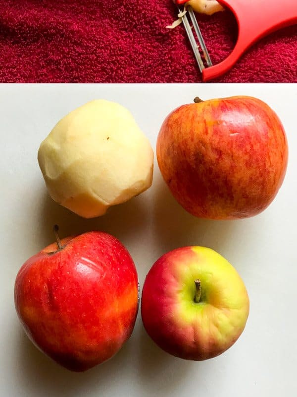 Four apples on a white cutting board.