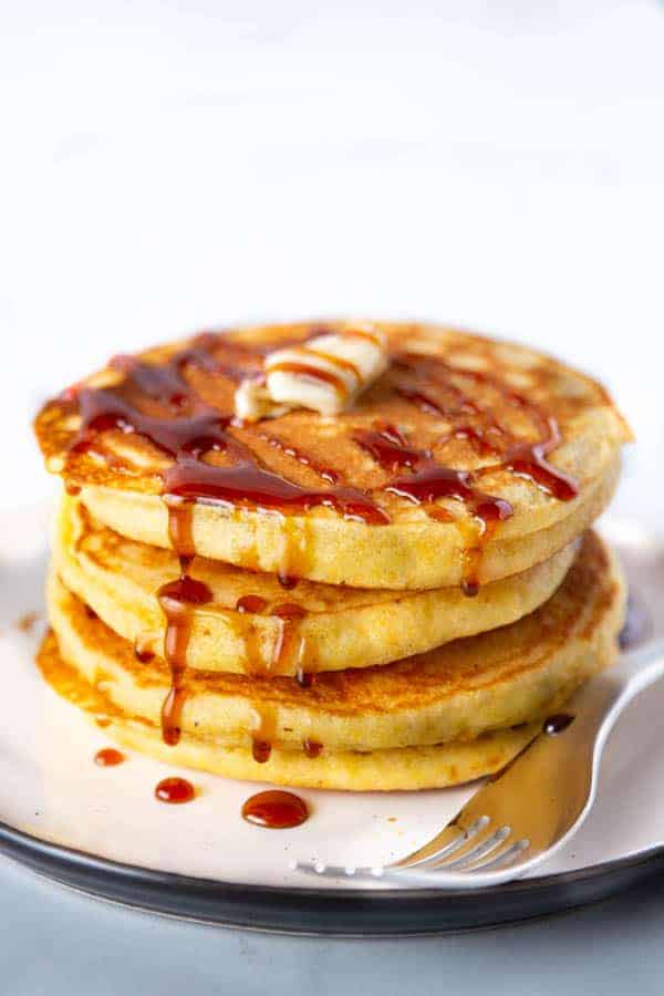 Tre pancake di farina di mais impilati su un piatto con sciroppo d'acero e burro.