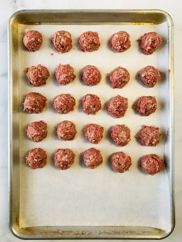 Uncooked meatballs on baking sheet.