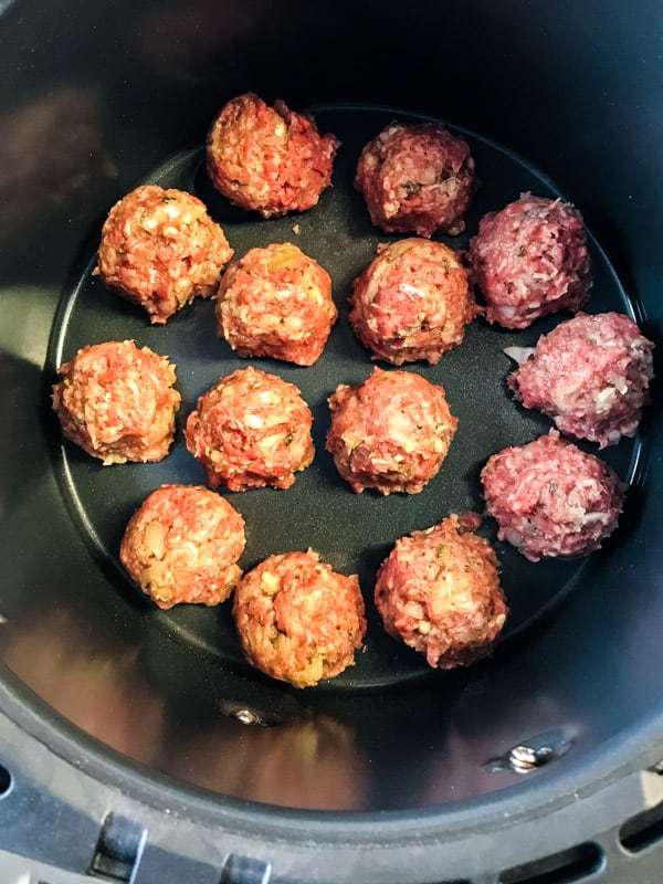 Uncooked meatballs in the tray of an air fryer.