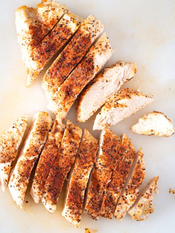 Air fryer chicken breast, cooked and sliced on cutting board.