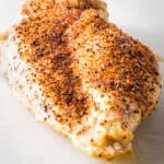 A cooked air fried chicken breast on a cutting board.