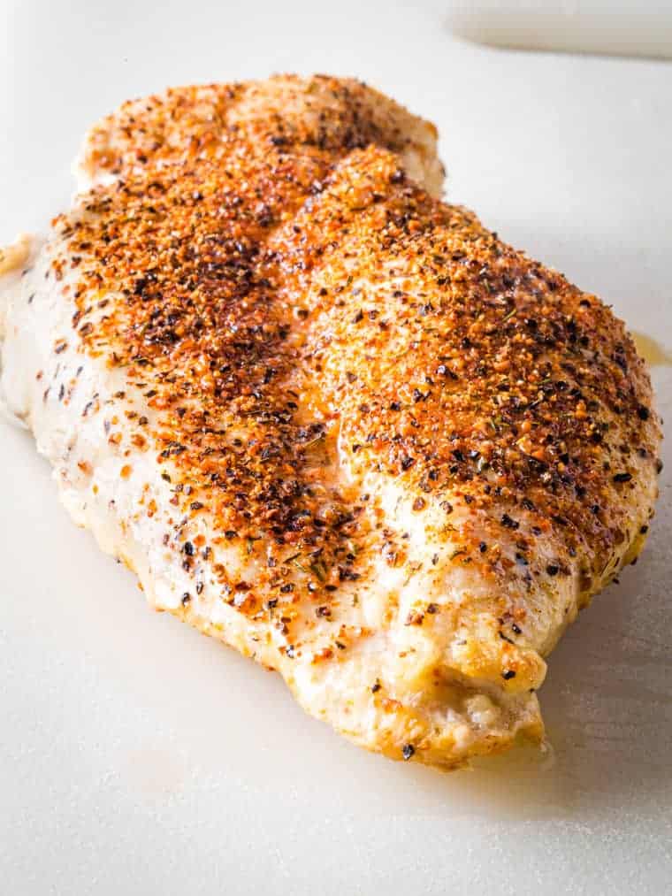 A cooked air fried chicken breast on a cutting board.