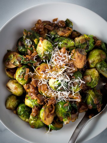 Bowl of Sauteed Brussels sprouts topped with parmesan cheese.