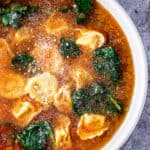 Bowl of tortellini soup with spinach topped with grated parmesan cheese.