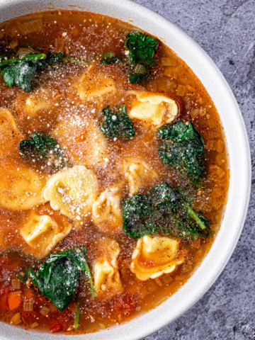 Bowl of tortellini soup with spinach topped with grated parmesan cheese.