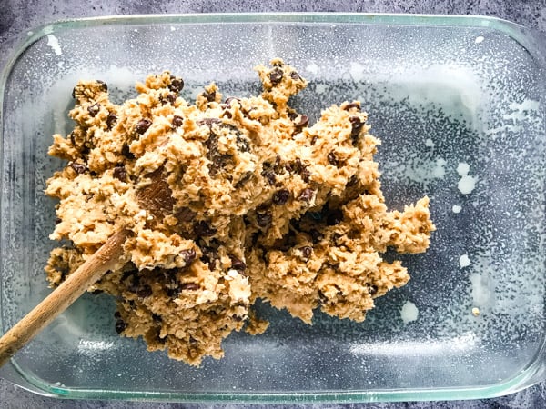 Oatmeal chocolate chip cookie dough being pressed into a greased pan with a wooden spoon.