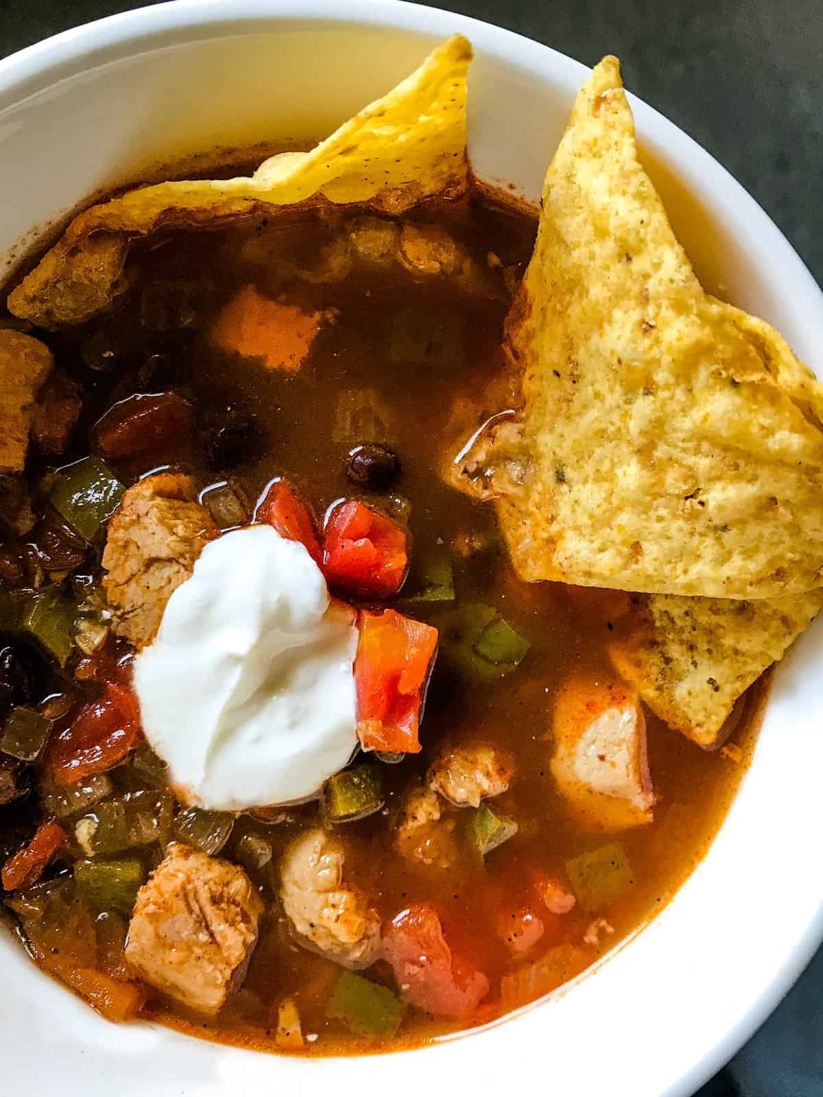 Chicken tortilla soup in white bowl with tortilla chips. 