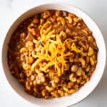 Chili Mac in a white bowl topped with grated Cheddar cheese.