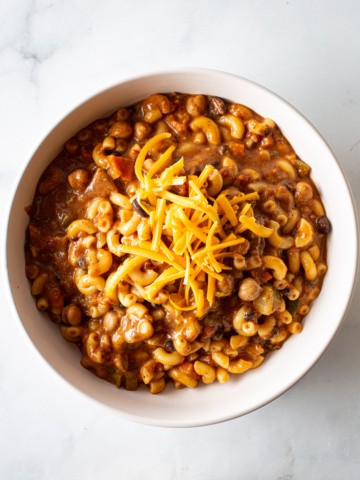 Chili Mac in a white bowl topped with grated Cheddar cheese.
