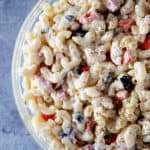 Bowl of macaroni salad with black olives, red peppers, and topped with black pepper.