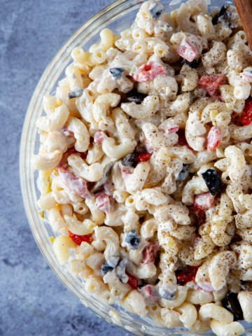 Bowl of macaroni salad with black olives, red peppers, and topped with black pepper.