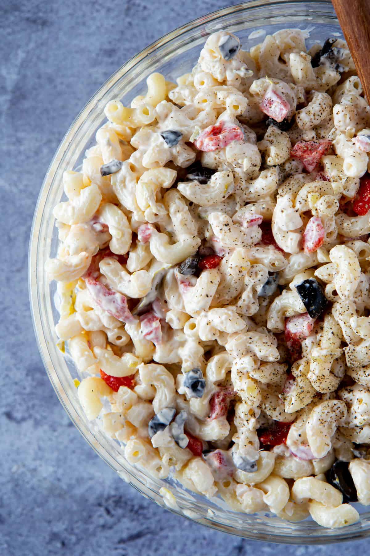 Bowl of macaroni salad with black olives, red peppers, and topped with black pepper.