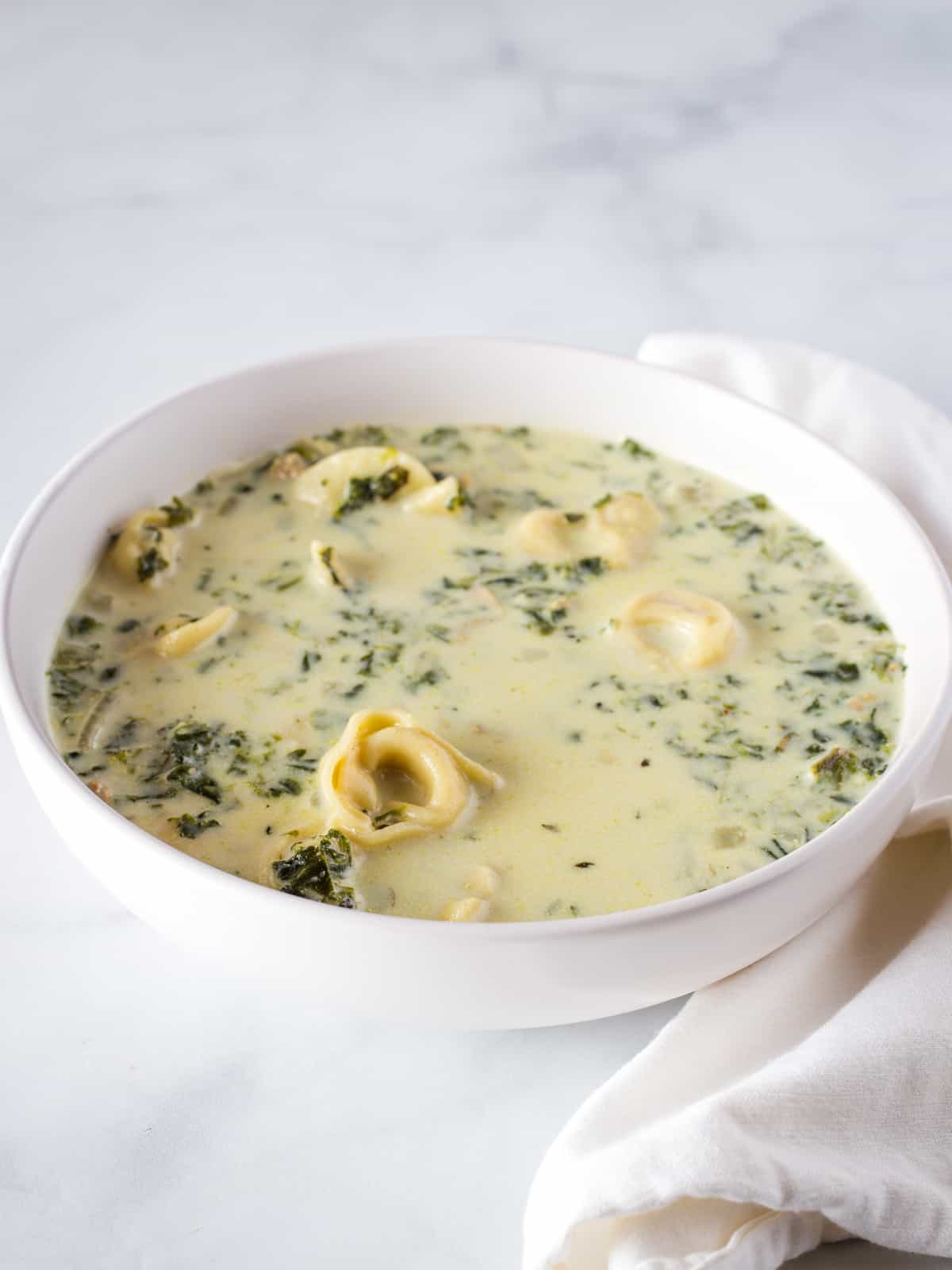 Creamy spinach and tortellini soup in bowl.