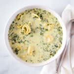 Creamy spinach and tortellini soup in bowl with spoon sitting alongside.
