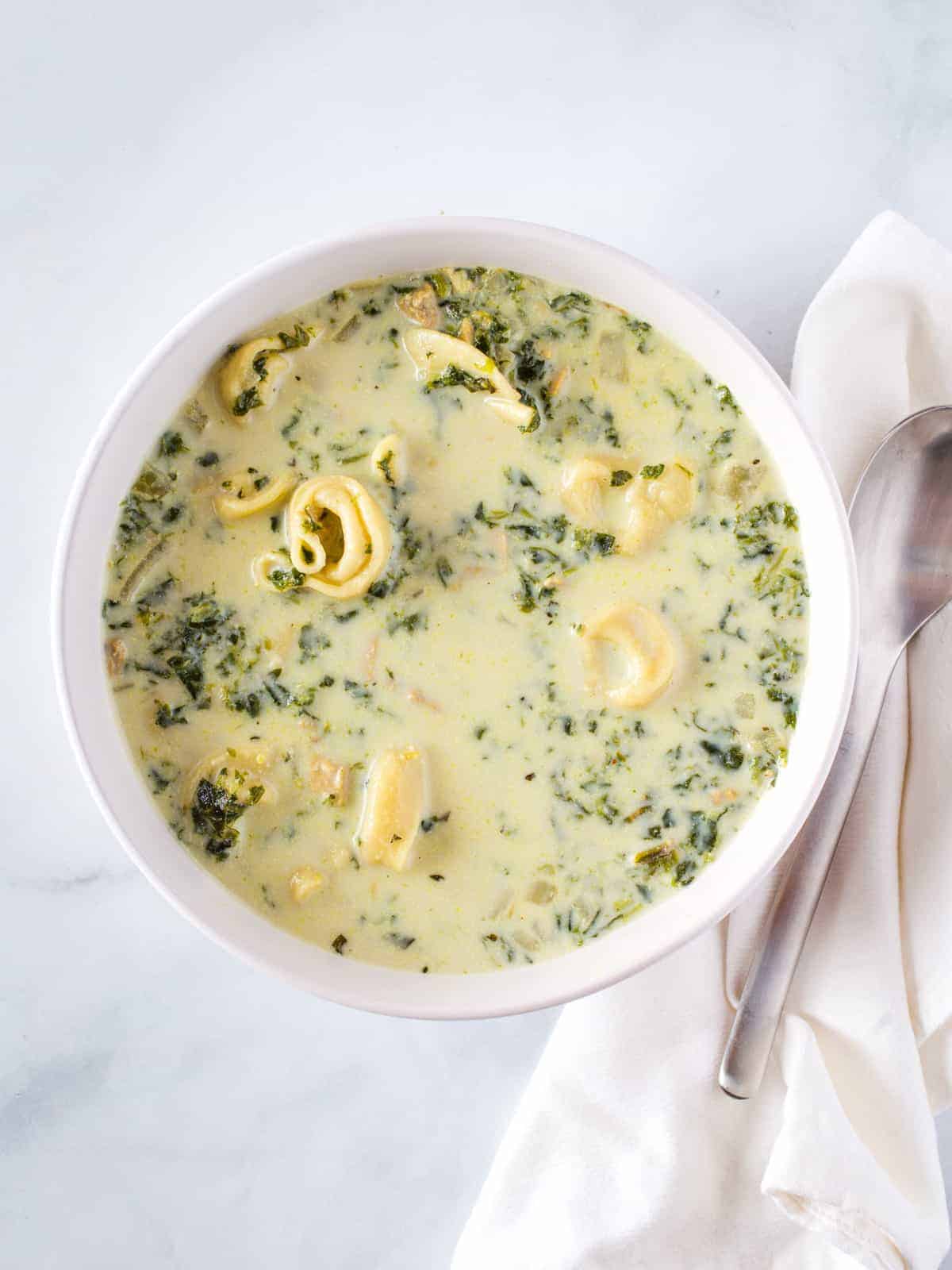 Creamy spinach and tortellini soup in bowl with spoon sitting alongside.