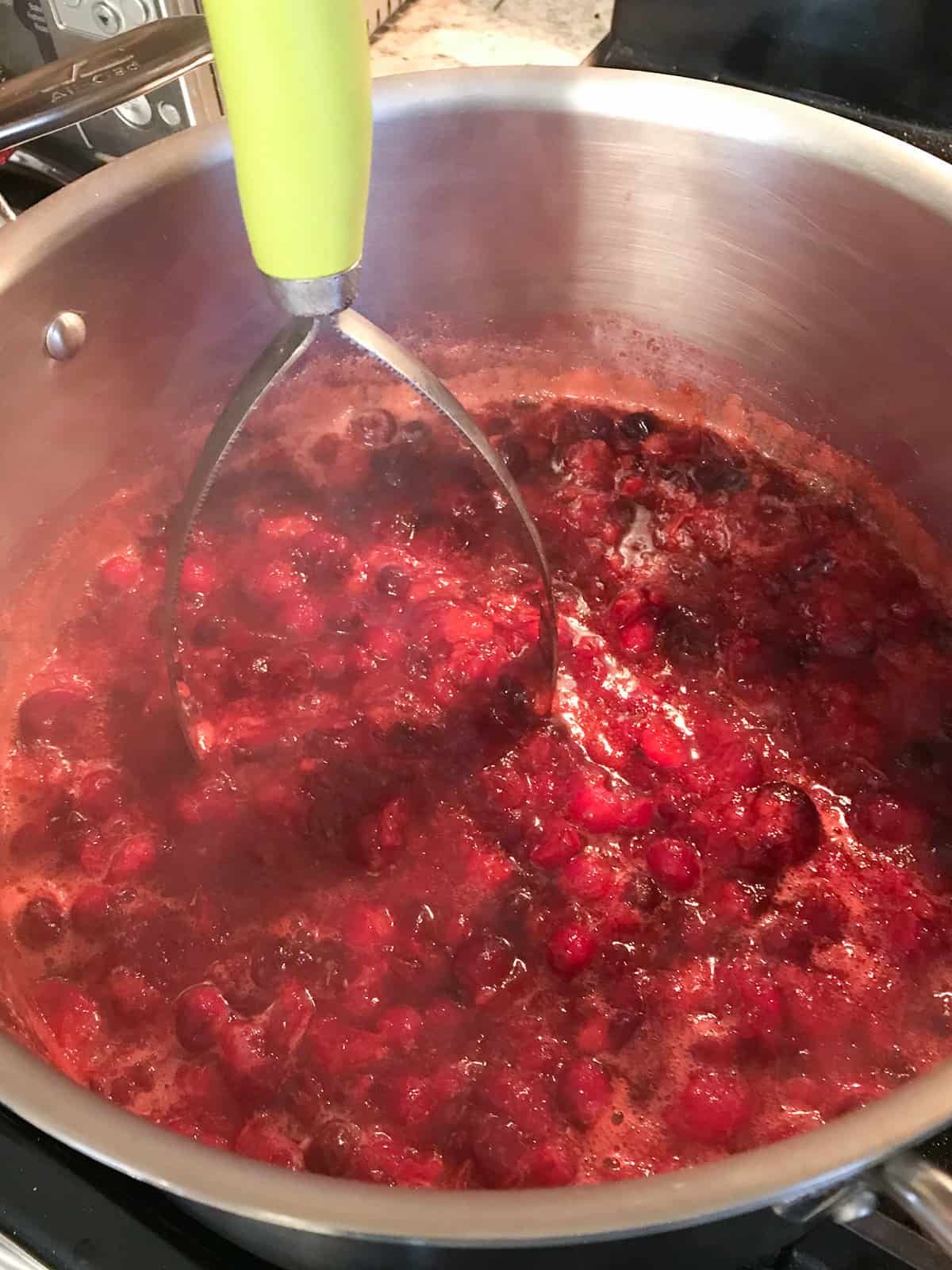 Mashing cooked cranberries with a potato masher.