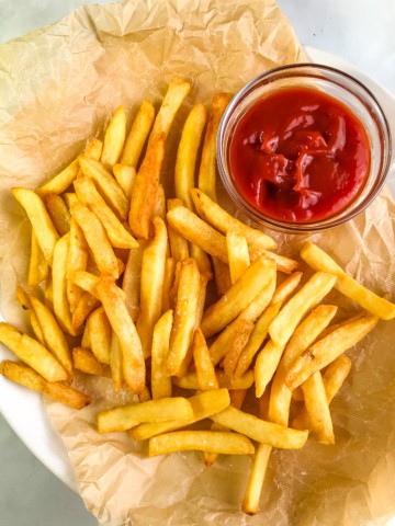 Air fryer cooked French fries on a platter with a small bowl of ketchup.