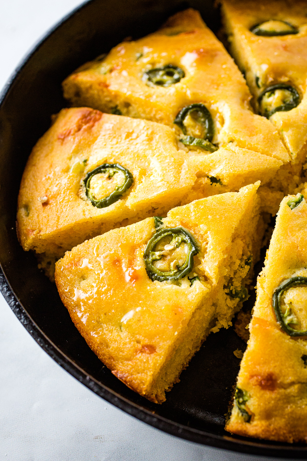 Baked cheddar jalapeno cornbread sliced in a skillet.