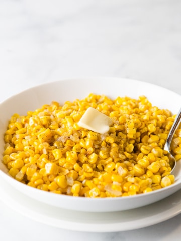 Cooked frozen corn with onions and black pepper, topped with butter, in a white bowl.
