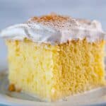 Slice of tres leches cake with whipped cream frosting on plate.