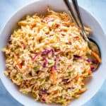 Easy coleslaw in a white bowl with two servings spoons alongside.