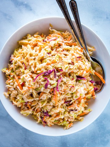 Easy coleslaw in a white bowl with two servings spoons alongside.