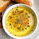 White bowl of bread dipping oil. Slices of bread are on the plate beside the oil.
