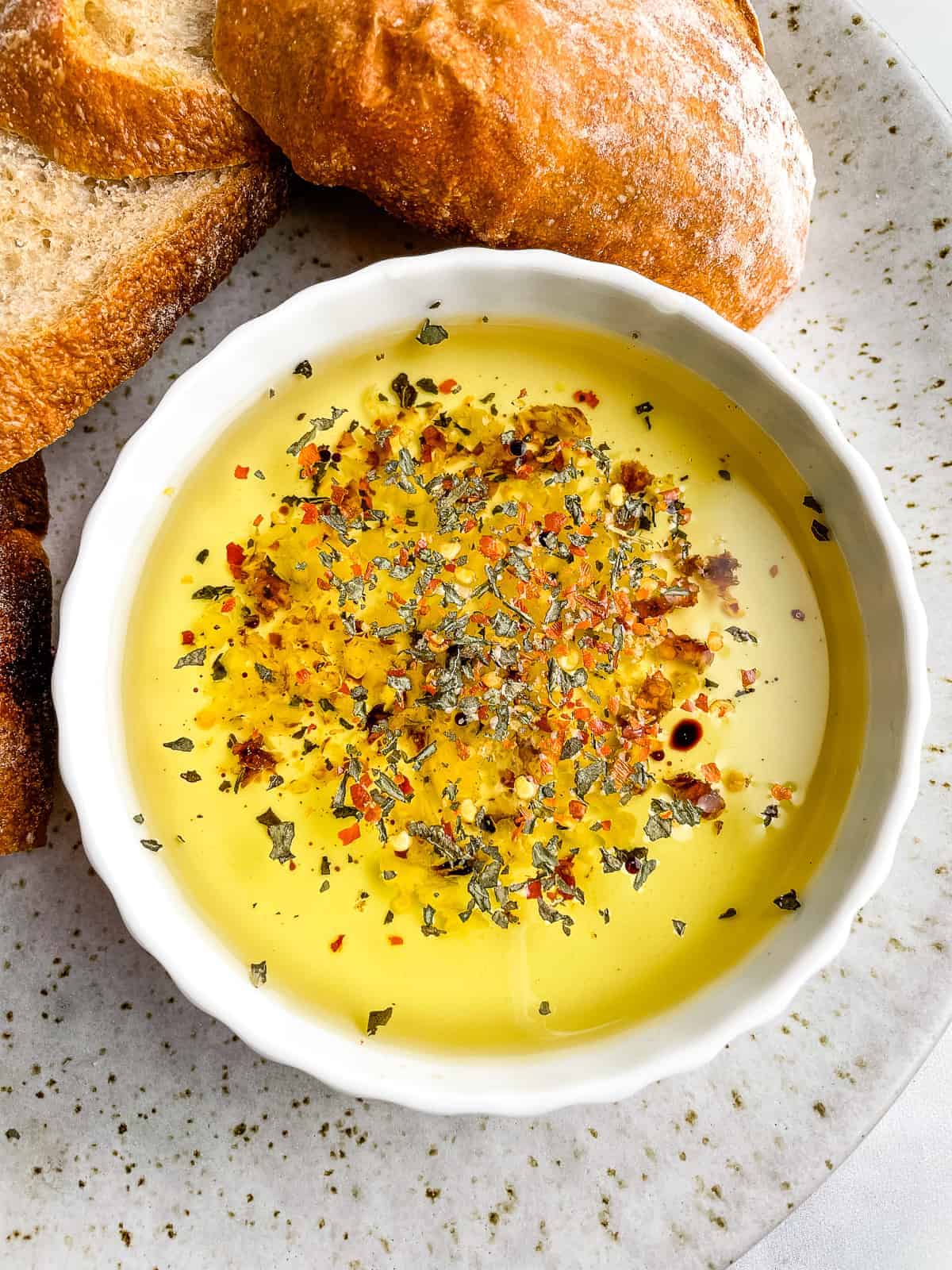 White bowl of bread dipping oil. Slices of bread are on the plate beside the oil.