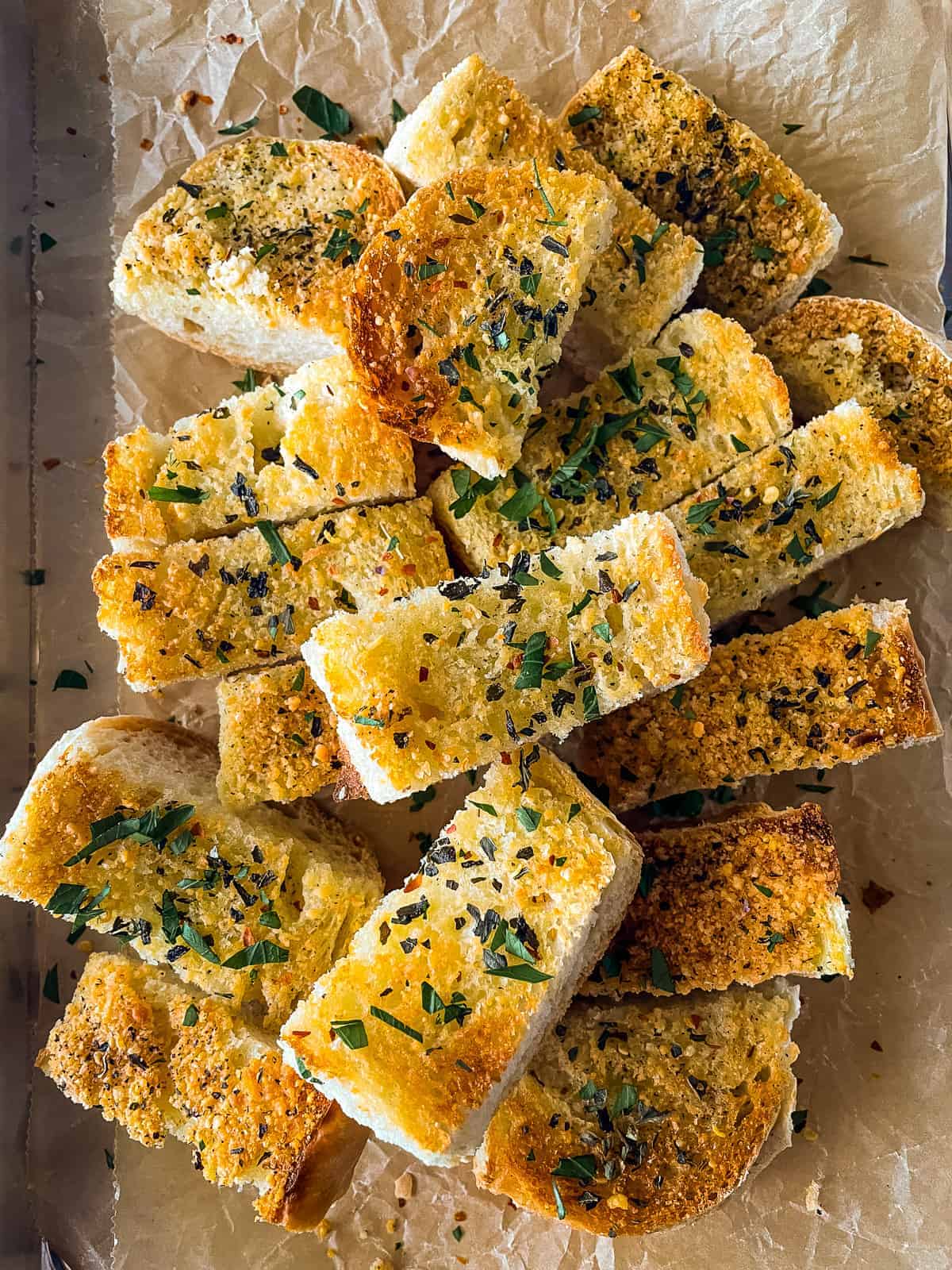 Sliced garlic bread on pan. Topped with fresh chopped parsley.