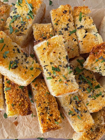 Garlic bread on a pan with herbs sprinkled on top.