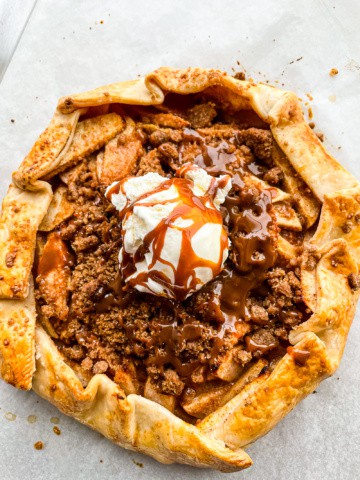 Apple galette on a baking sheet topped with ice cream and a drizzle of caramel sauce.