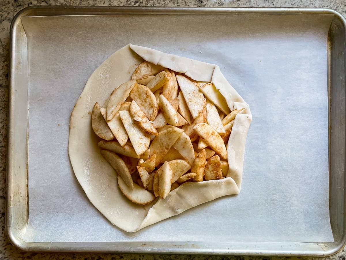 Filled apple galette with pie crust being folded over filling.