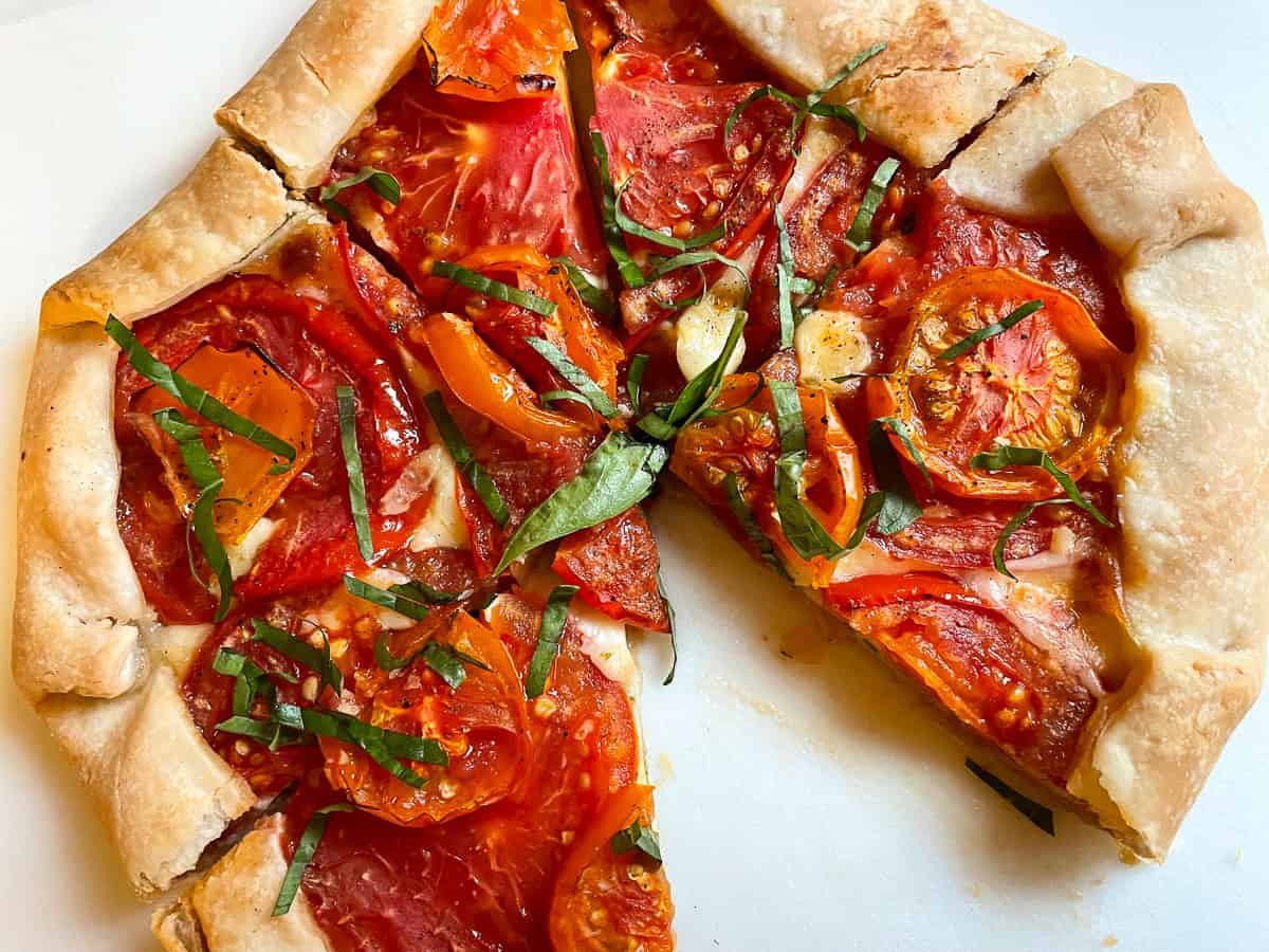 Tomato galette, topped with fresh basil, on cutting board.