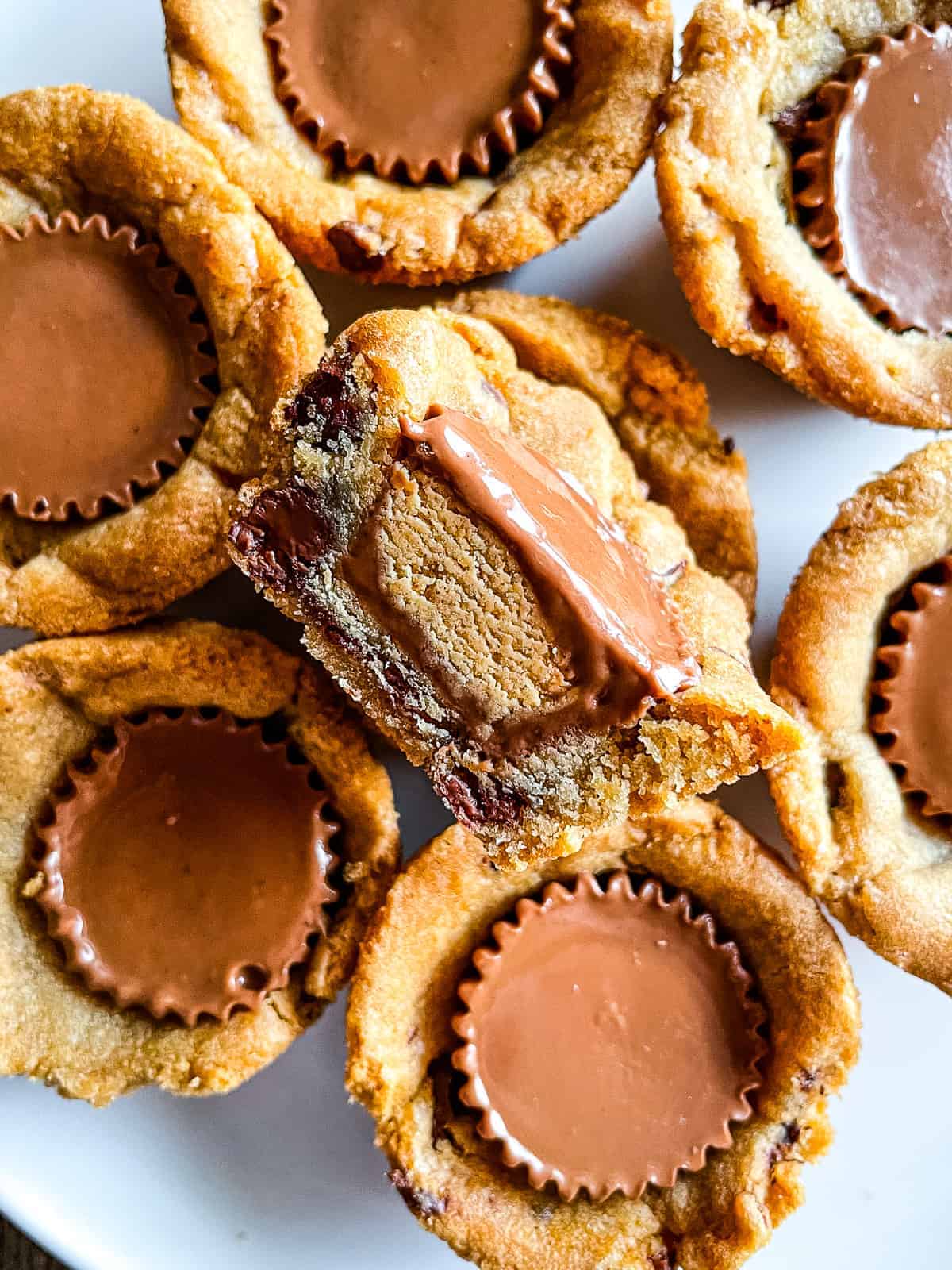 Chocolate chip peanut butter cup cookies on a white plate. One cookie is cut in half to show the peanut butter cup filling.