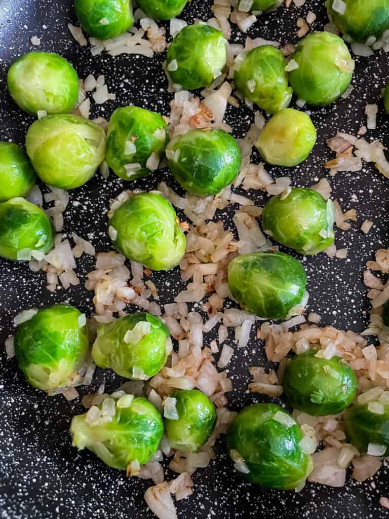 Thawed Brussels sprouts in a skillet with cooked onions.