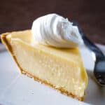 Slice of lemon pie topped with whipped cream on plate.