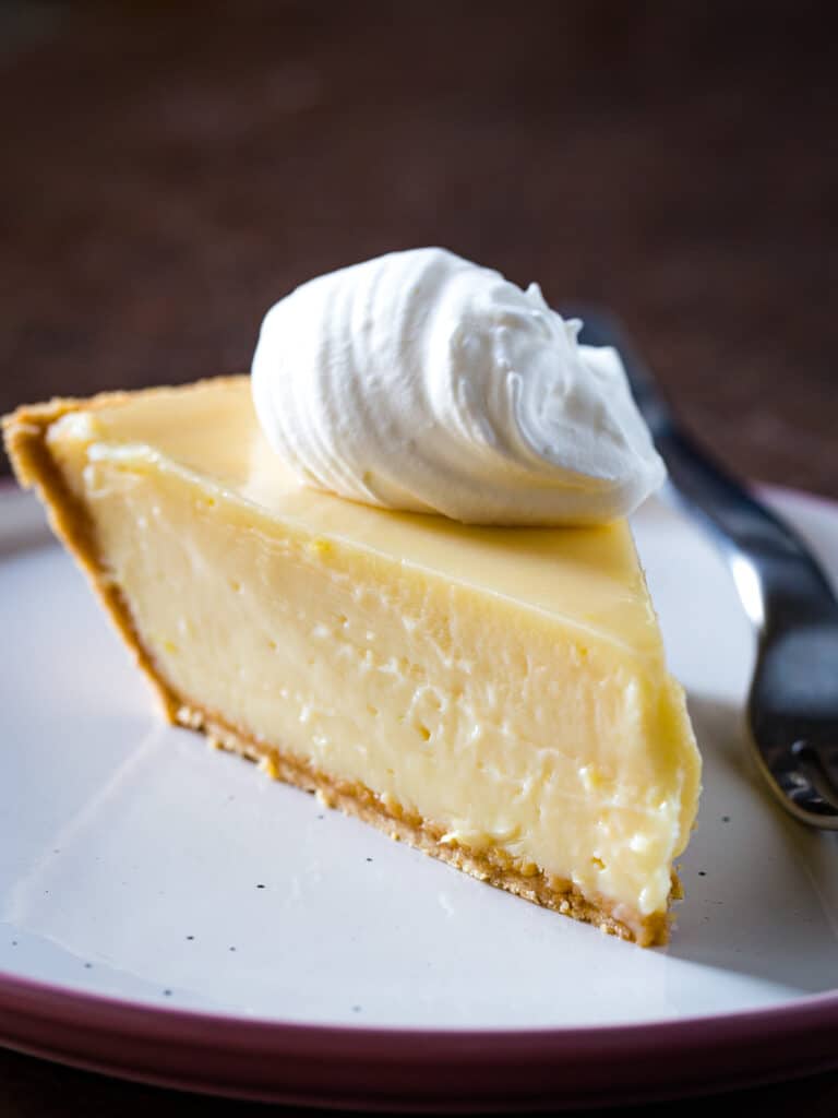 Slice of lemon pie topped with whipped cream on plate.