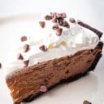 Slice of chocolate mousse pie, topped with whipped cream and chocolate chips on a plate.