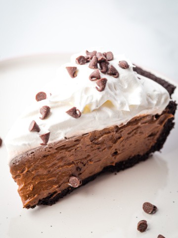 Slice of chocolate mousse pie, topped with whipped cream and chocolate chips on a plate.