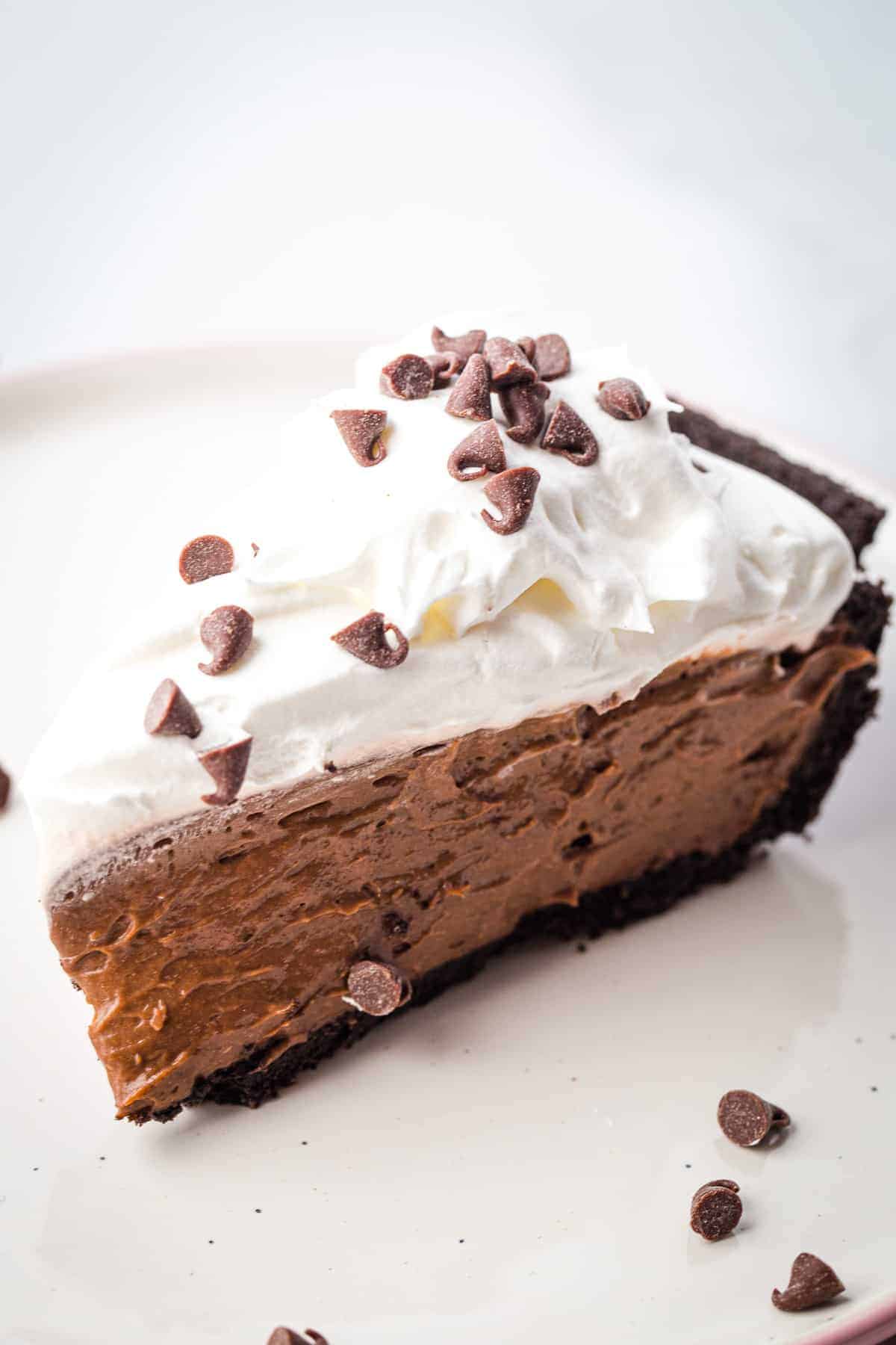 Slice of chocolate mousse pie, topped with whipped cream and chocolate chips on a plate.