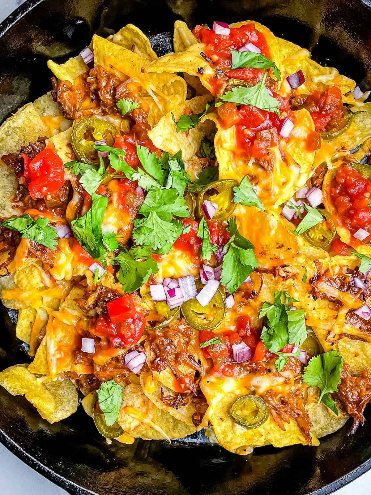 Cast iron skillet filled with pulled pork nachos. 