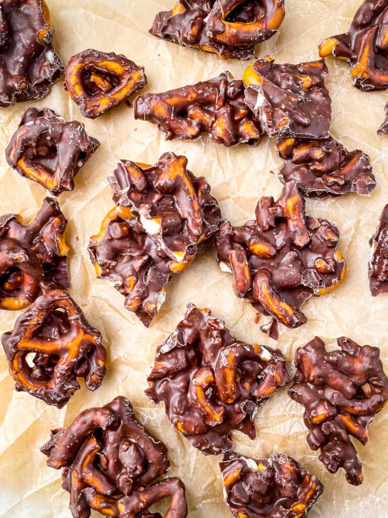 Chocolate covered pretzel bark broken into pieces on brown parchment.
