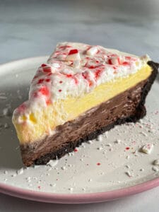 Peppermint bark pie on a plate. Bottom layer is chocolate. Top layer vanilla. Finished with whipped cream and crushed candy canes.