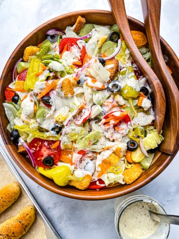 Large Italian salad drizzled with creamy Italian dressing. Pan of breadsticks and jar of dressing on the side.