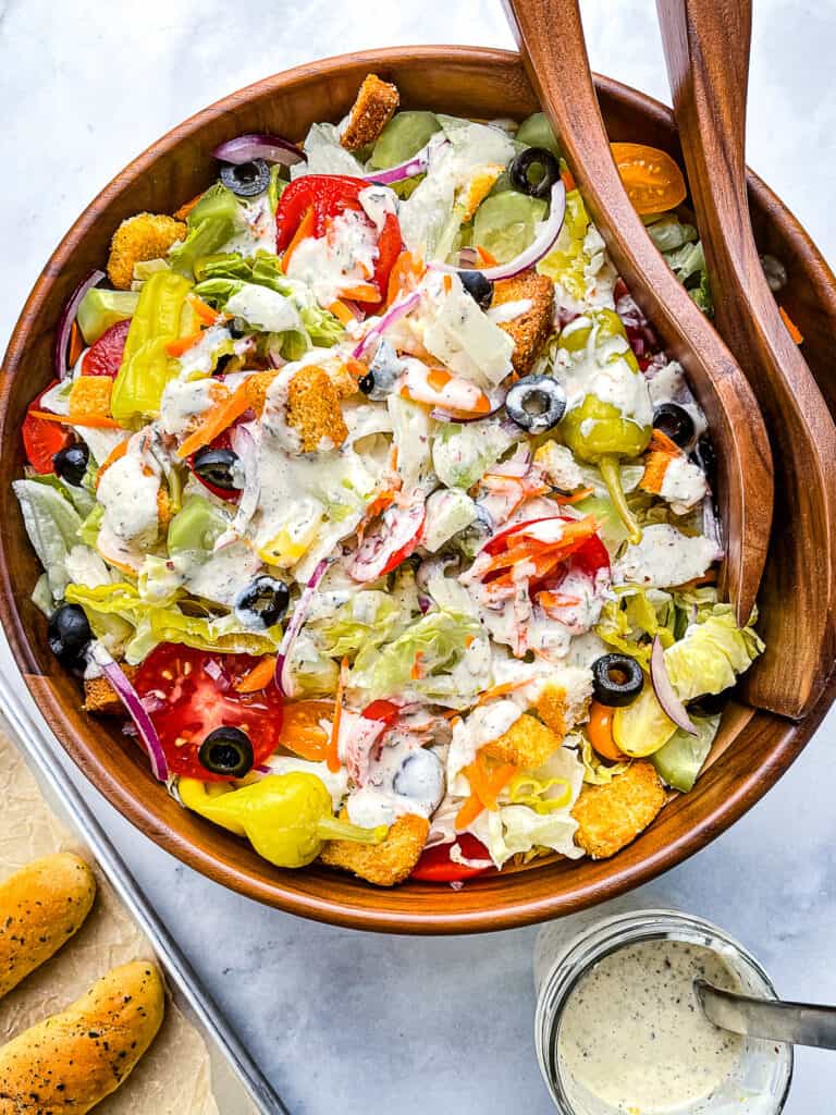 Large Italian salad drizzled with creamy Italian dressing. Pan of breadsticks and jar of dressing on the side.