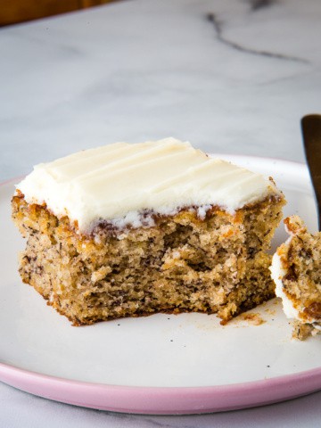 Slice of banana cake topped with cream cheese frosting on a plate.
